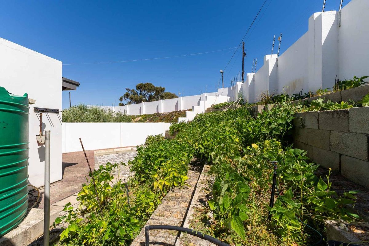 A rear garden area featuring tiered retaining walls, a paved section, and a large water storage tank against a high perimeter wall.