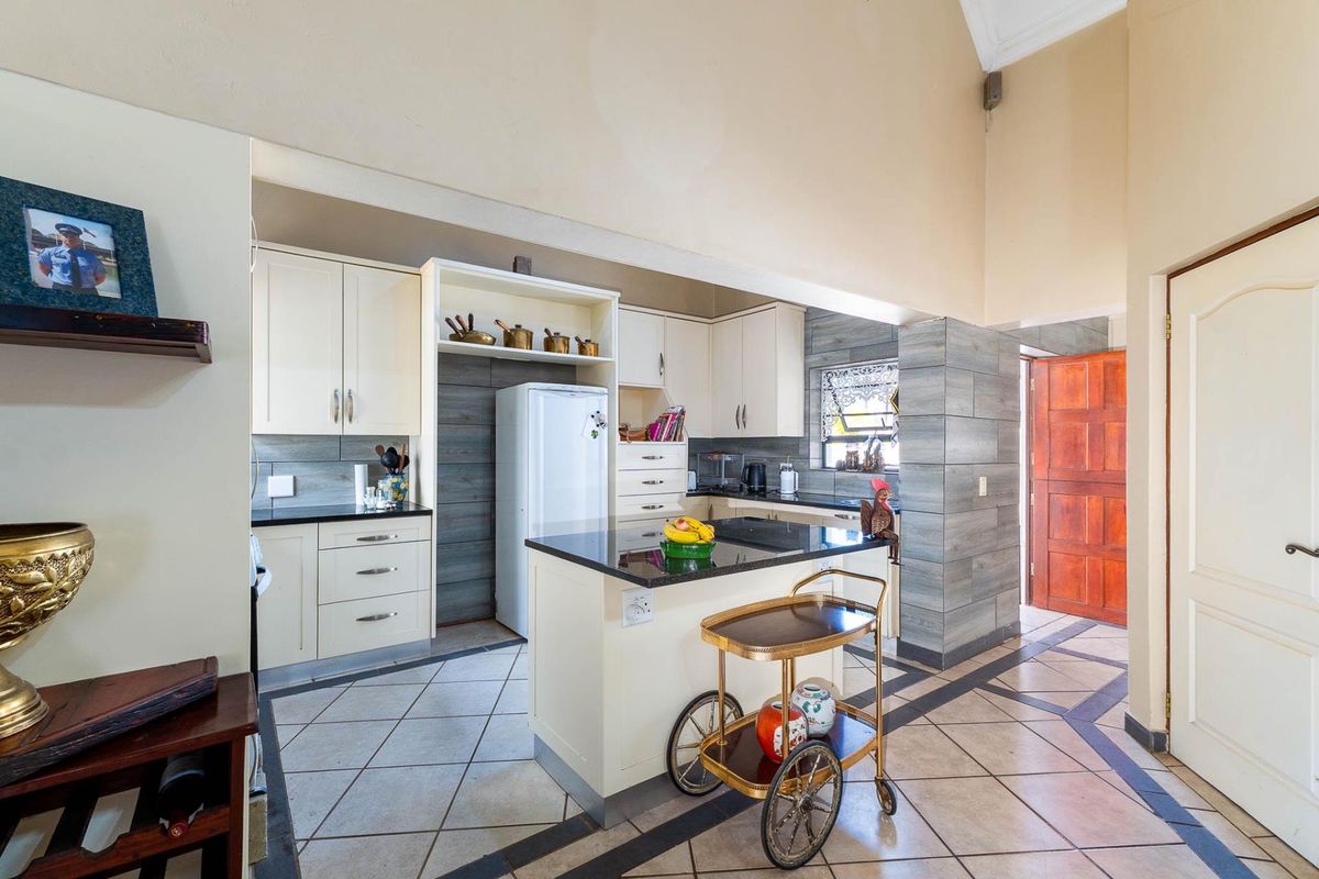 A well-lit kitchen featuring cream cabinetry, dark granite countertops, a central island, and modern grey tiled wall accents with high vaulted ceilings.