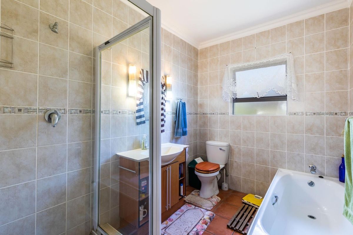 A functional bathroom featuring a glass-enclosed shower, a built-in vanity with basin, a toilet, and a bathtub with full-height wall tiling.