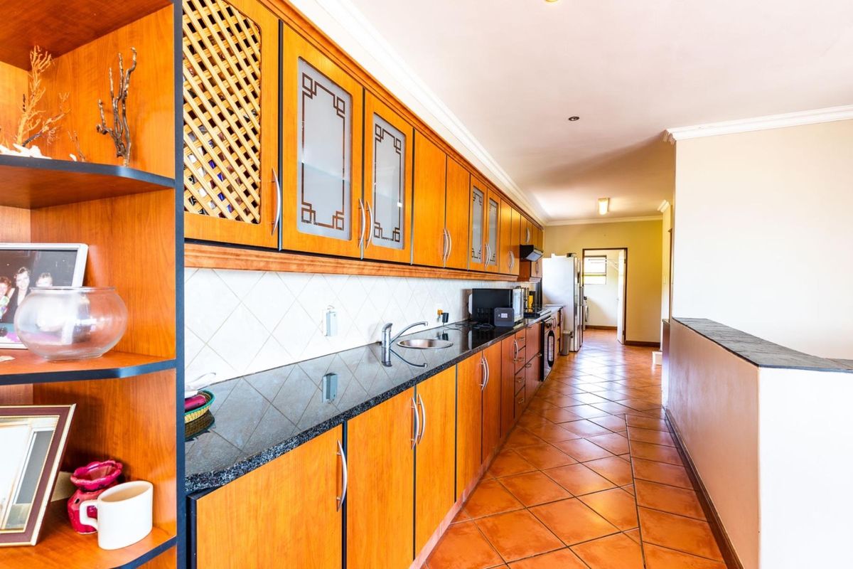 A functional kitchen featuring wooden cabinetry, dark granite countertops, and tiled flooring, offering a practical layout with ample storage space.