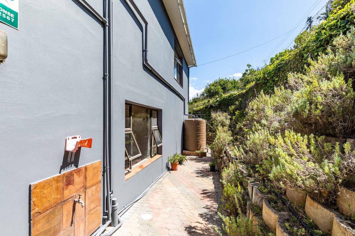 Side exterior view of the property featuring a paved walkway, water storage tank, and a terraced garden wall.