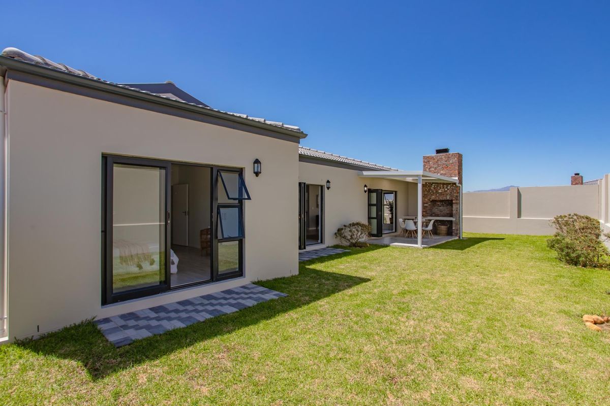 Rear view of the property featuring a landscaped garden, paved patio area, and a built-in brick braai fireplace.