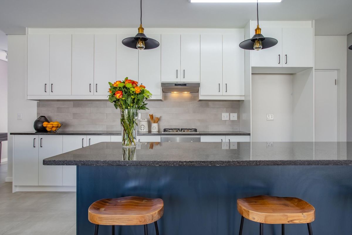 Modern kitchen featuring white cabinetry, dark stone countertops, a central island, stainless steel gas hob, extractor fan, and tiled backsplash.