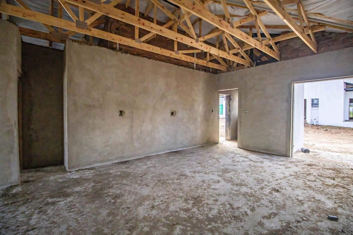 An interior view of a townhouse under construction, featuring exposed timber roof trusses, raw plastered walls, and unfinished concrete flooring.