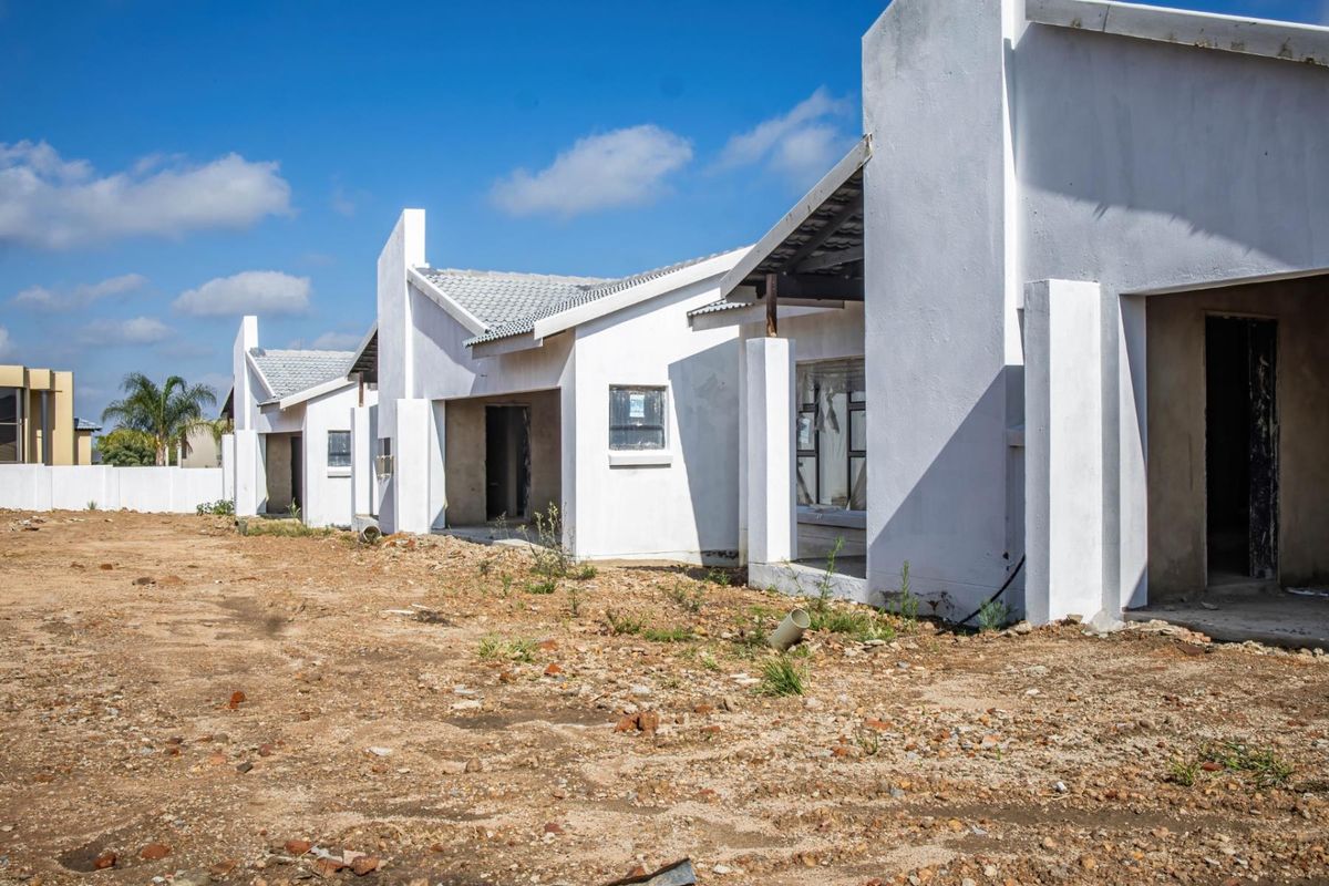 A row of newly constructed townhouse units featuring white plastered facades, tiled roofs, and unfinished surrounding grounds awaiting final landscaping.