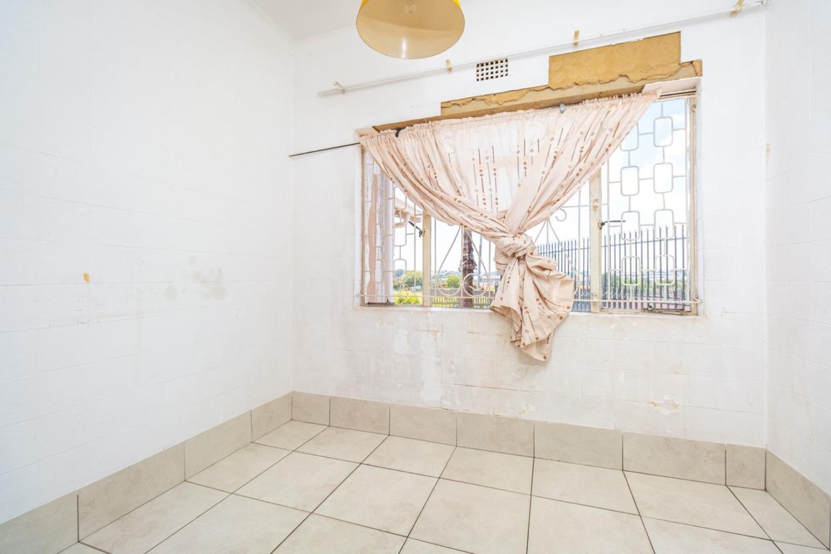 An empty room featuring tiled flooring and a window with security bars, requiring cosmetic repairs to the wall surface above the window frame.