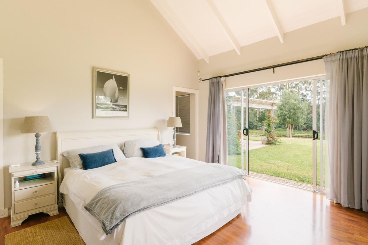 Spacious bedroom featuring high vaulted ceilings, timber flooring, and large sliding glass doors providing direct access to the garden and patio area.