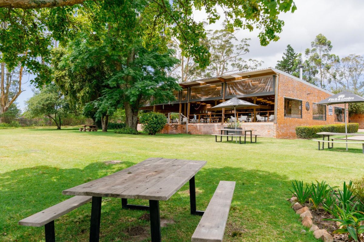 A view of the farm property featuring a brick building with a covered patio area set within a spacious, well-maintained garden.