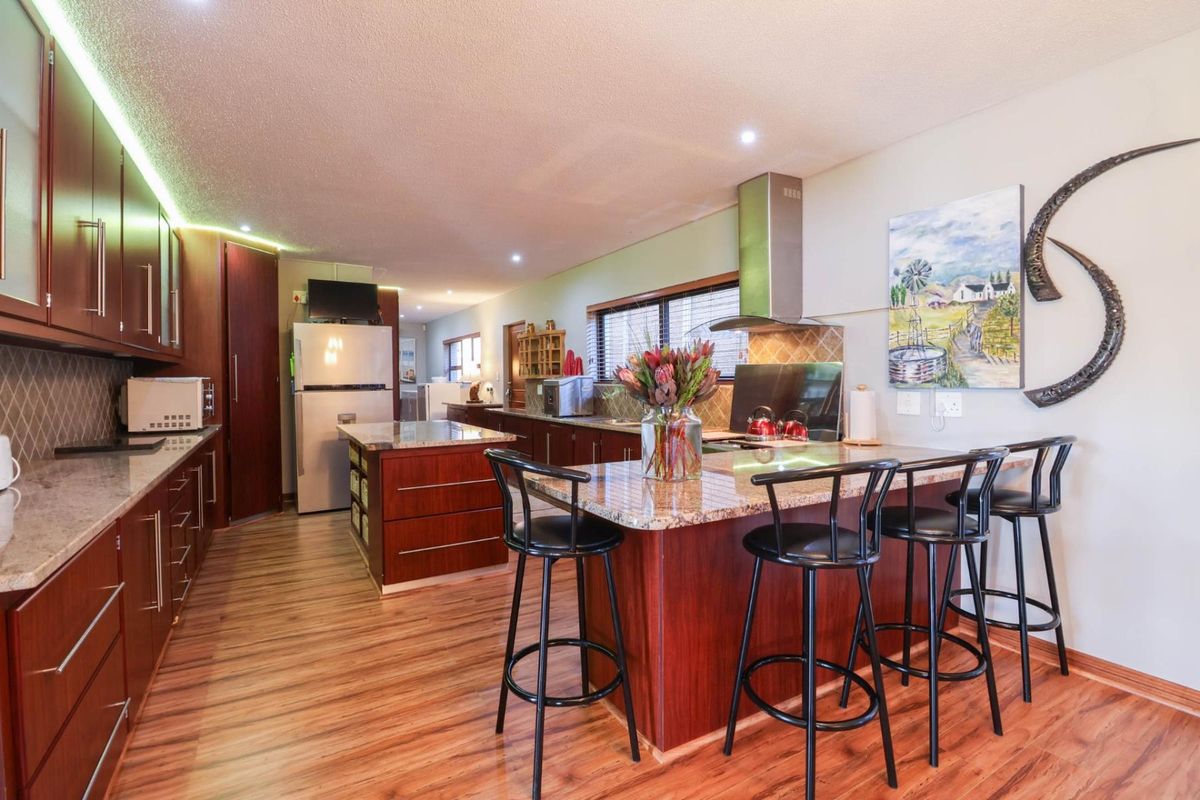 Spacious kitchen featuring dark wood cabinetry, granite countertops, a central island with breakfast bar seating, and a stainless steel extractor fan.