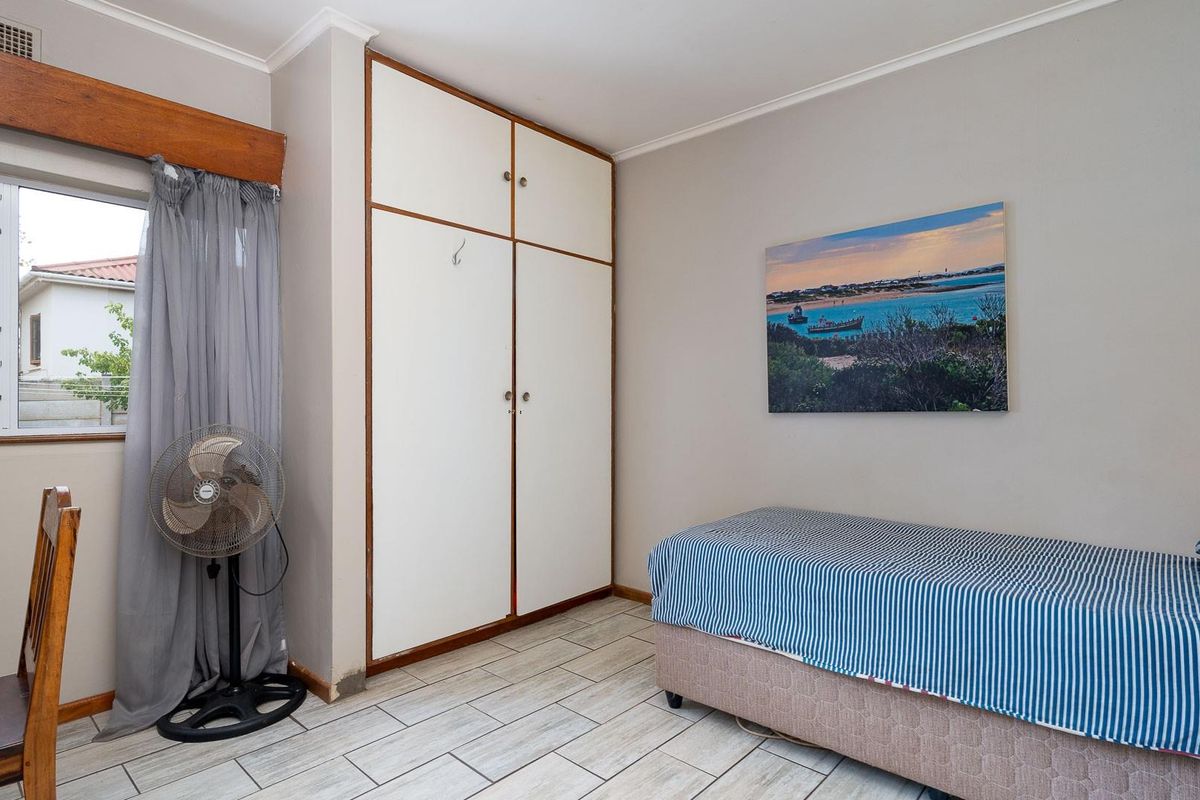 A functional bedroom featuring built-in cupboards, tiled flooring, and a window providing natural light.