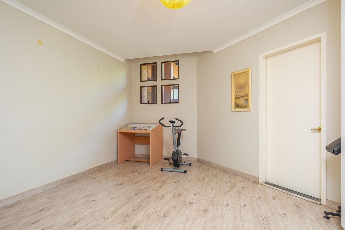A versatile room featuring light wood-look flooring, neutral walls, and a set of small square windows, suitable for use as a bedroom or home office.