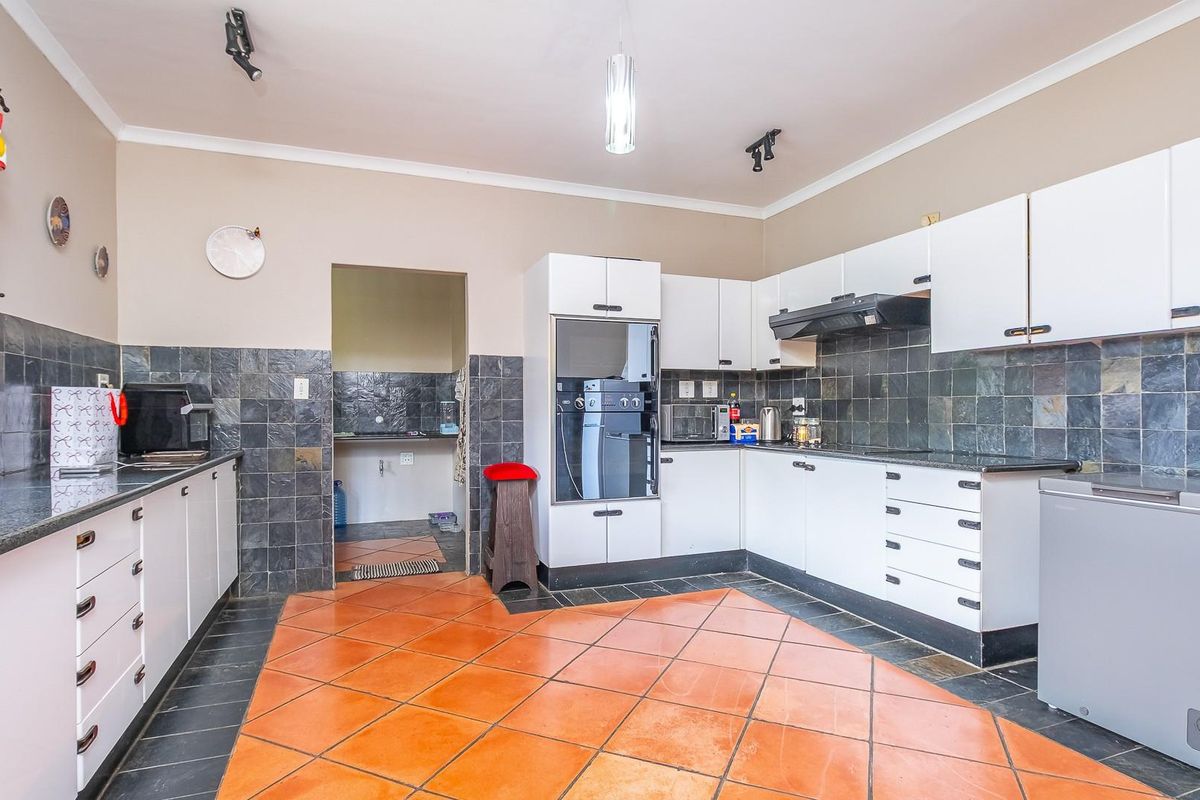 A functional kitchen featuring white cabinetry, dark stone-style wall tiles, built-in oven, extractor fan, and terracotta floor tiles, with an adjacent scullery area.