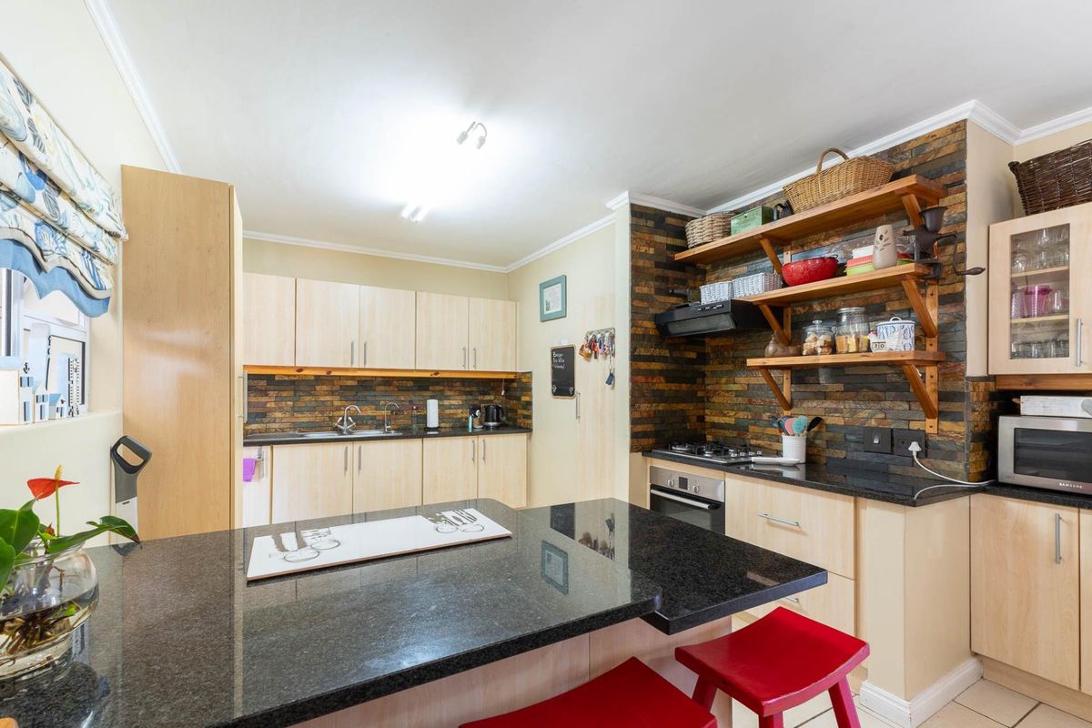 A functional kitchen featuring light wood cabinetry, black granite countertops, a stone-clad feature wall, and an integrated gas hob with an extractor fan.