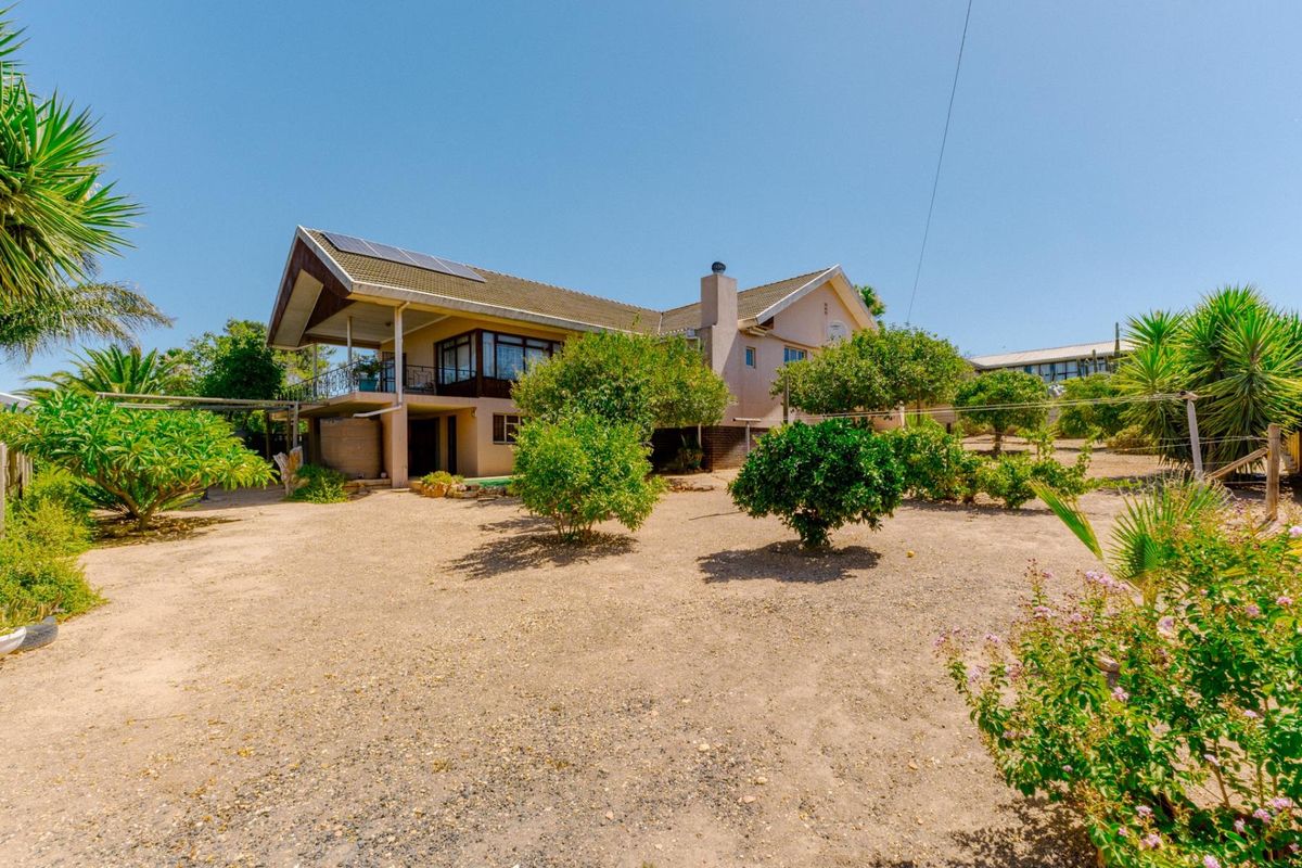 Rear view of a multi-level house featuring a covered balcony, solar panels, and a spacious, low-maintenance garden area with mature trees.