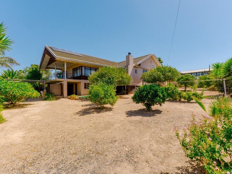 Rear view of a multi-level house featuring a covered balcony, solar panels, and a spacious, low-maintenance garden area with mature trees.