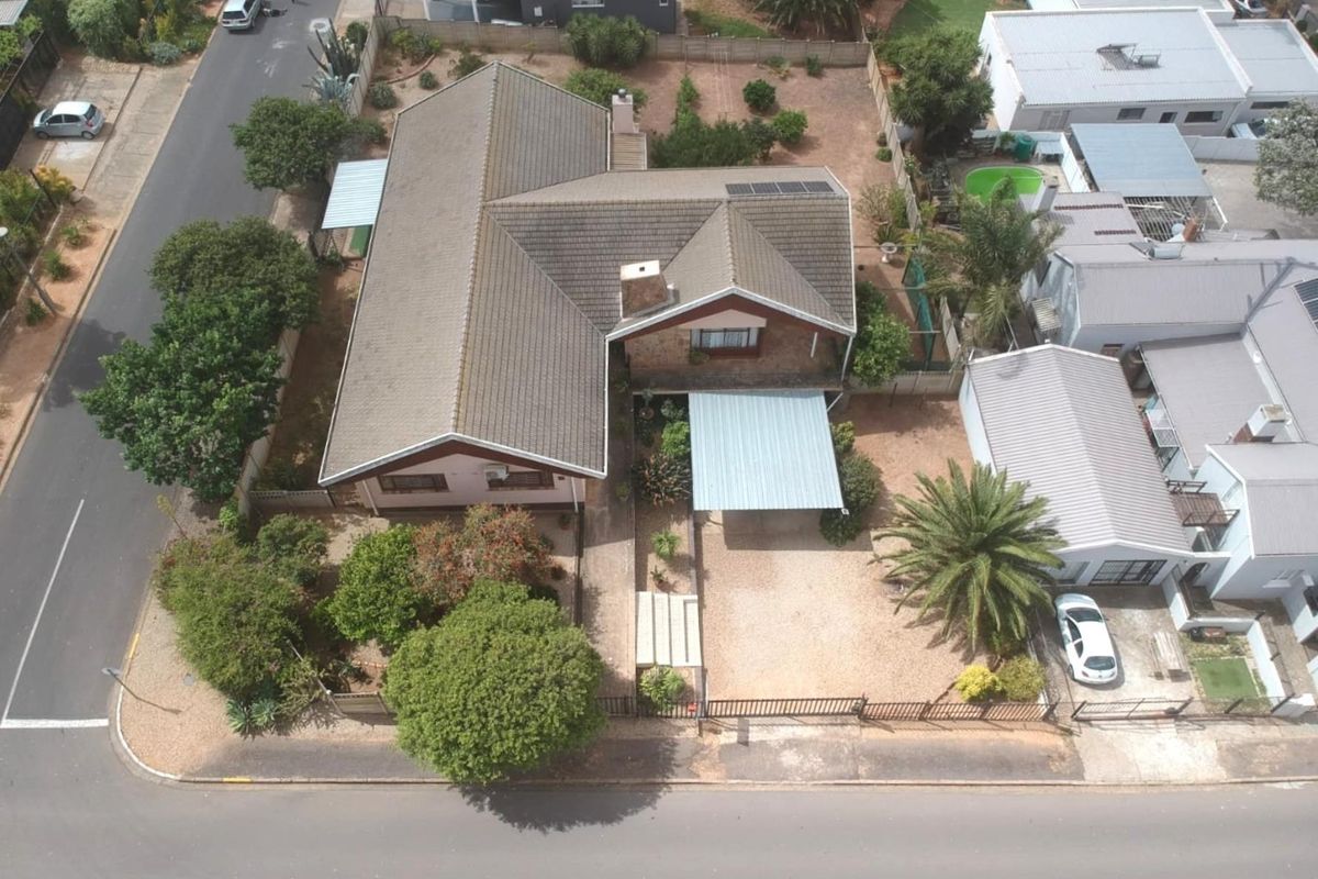 Aerial view of a residential property featuring a tiled roof, carport, and established garden on a corner plot.