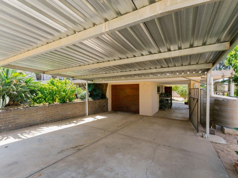 A covered carport area featuring a corrugated metal roof, concrete flooring, and a brick retaining wall, providing sheltered parking space.