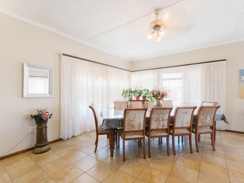 A bright dining room featuring neutral tiled flooring, large windows with sheer curtains, and a central ceiling fan.