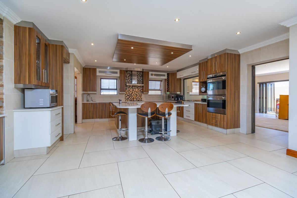 Modern kitchen featuring wood-grain cabinetry, a central island with breakfast bar, built-in double oven, and tiled flooring with recessed ceiling lighting.