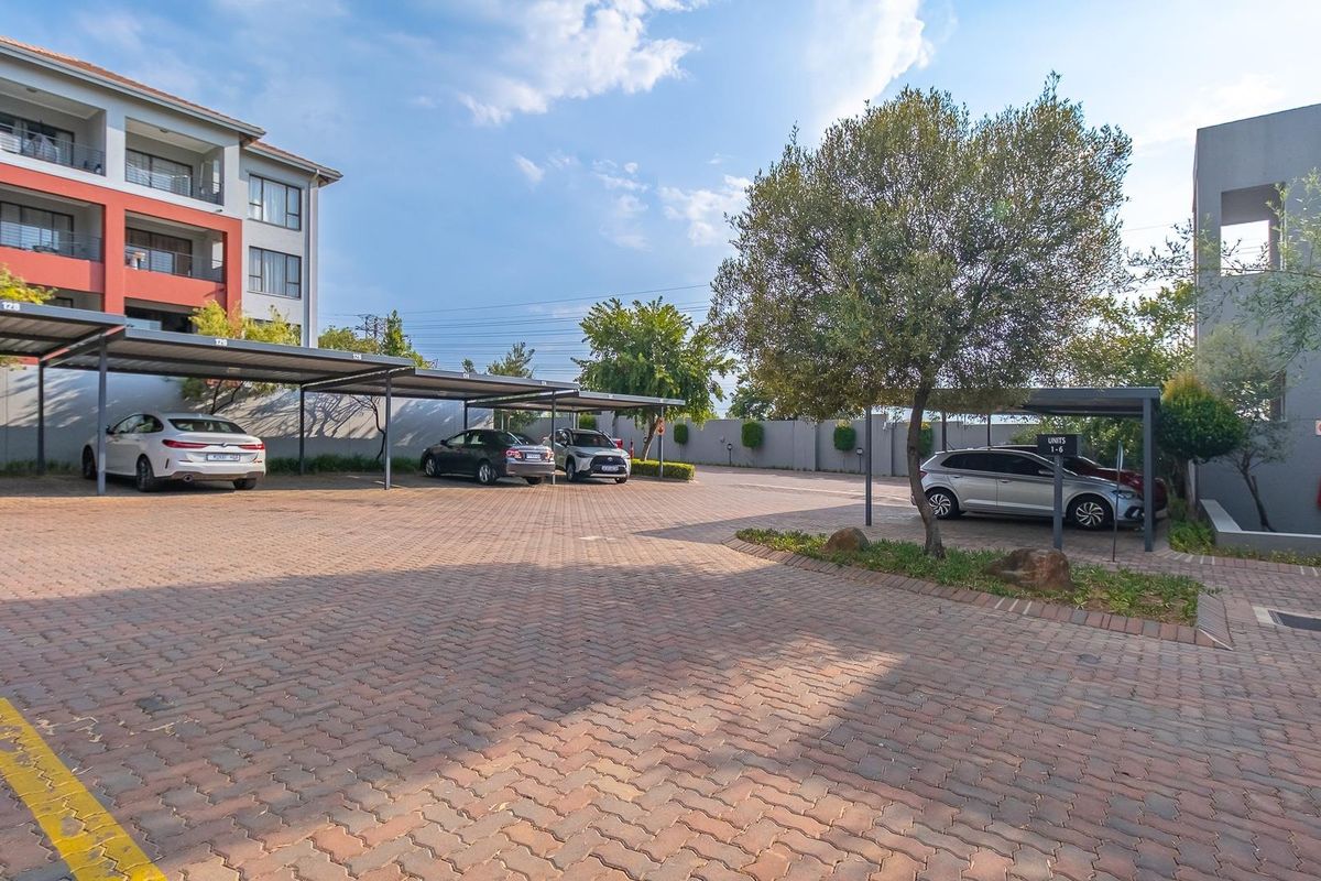 A well-maintained paved parking area featuring covered carports for residents, set within a modern apartment complex with landscaped surroundings.