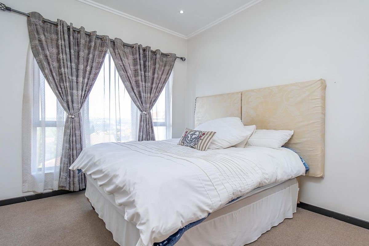 A well-lit bedroom featuring neutral carpeting, large windows with curtain tracks, and a clean, minimalist aesthetic.