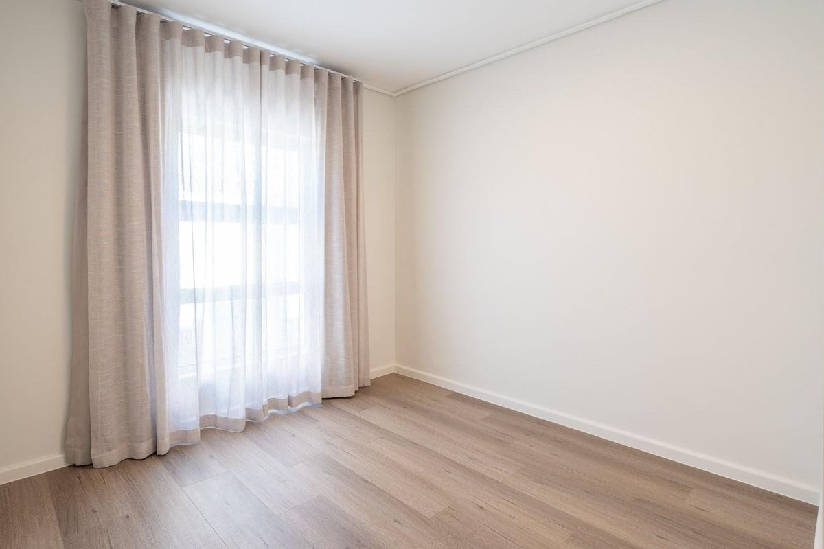 A bright, neutral bedroom featuring modern light wood-look flooring and floor-to-ceiling window treatments.