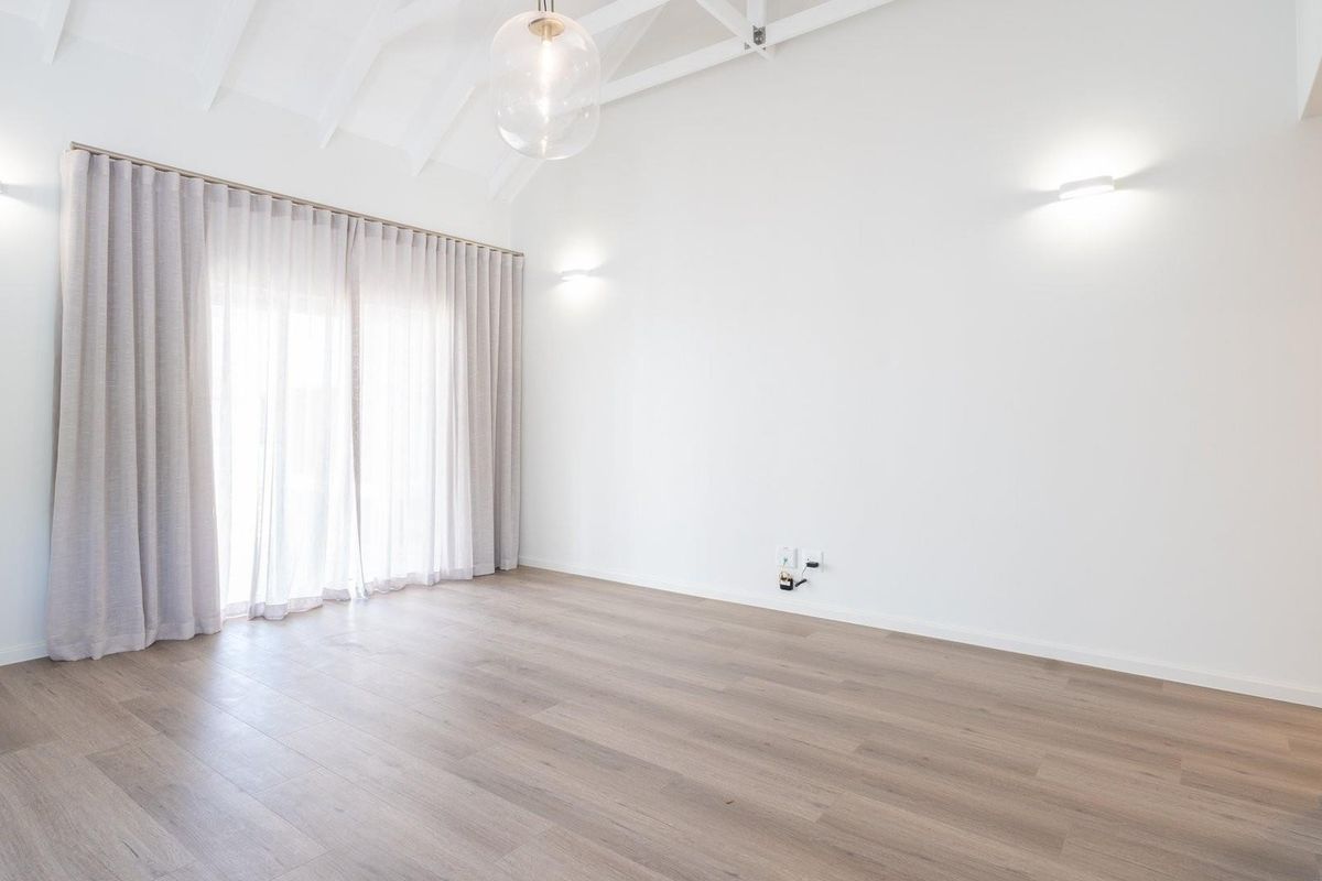 Bright and spacious living area featuring vaulted ceilings, modern wood-look flooring, and large sliding doors with elegant floor-to-ceiling curtains.