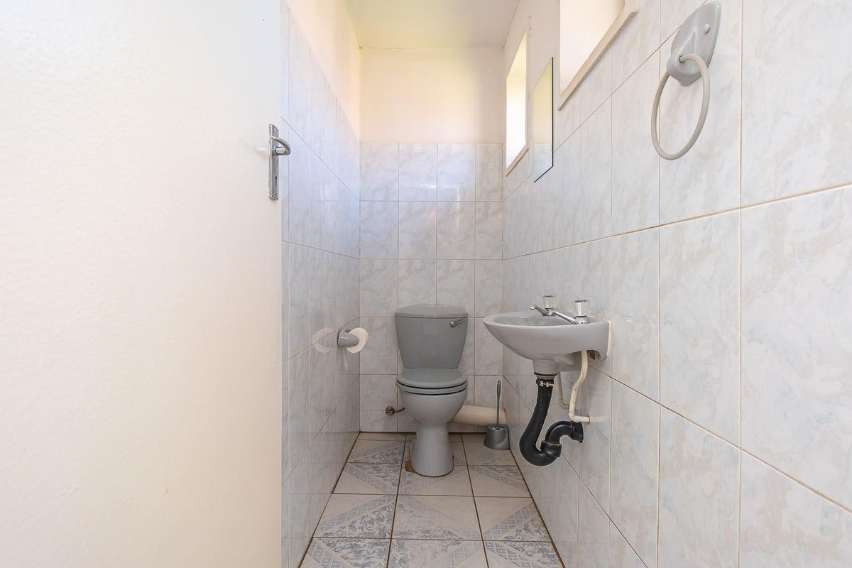 A compact office restroom featuring a standard toilet, wall-mounted basin, and full-height wall tiling.