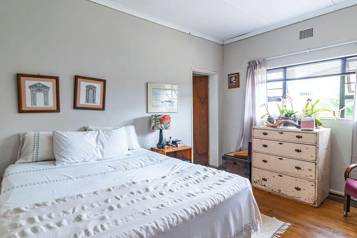 A bedroom featuring original wooden flooring, a large window allowing natural light, and a neutral wall finish.