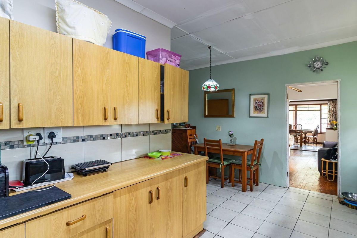A functional kitchen featuring light wood cabinetry, tiled splashbacks, and tiled flooring, with an open transition into the adjacent dining and living area.