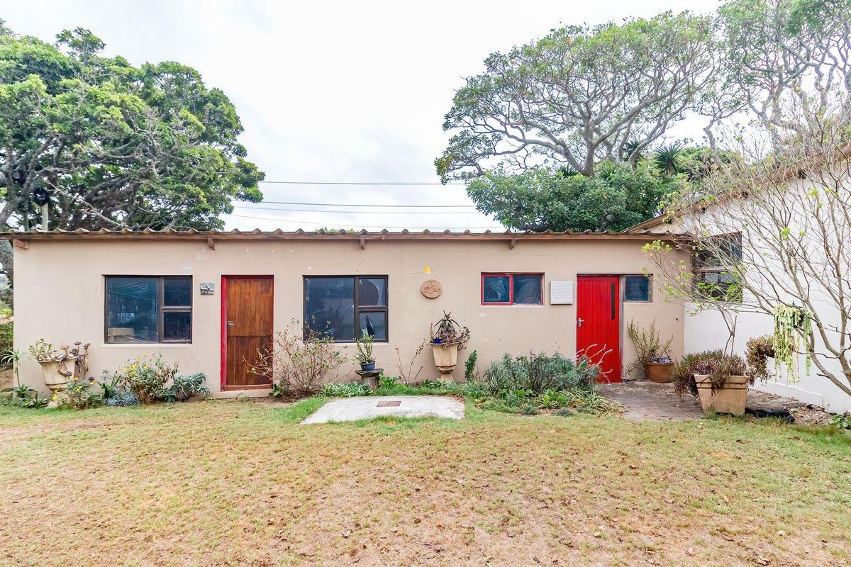 Rear view of the property featuring a single-story structure with multiple access points, set against a mature garden and established trees.