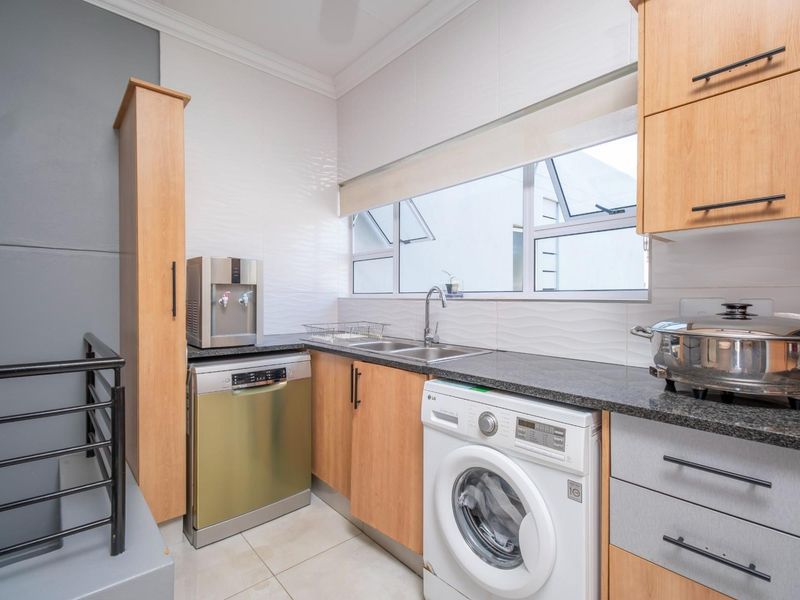 A functional kitchen featuring granite countertops, built-in cabinetry, a stainless steel sink, and dedicated space for a washing machine and dishwasher.