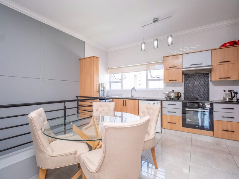 Modern open-plan kitchen and dining area featuring light wood cabinetry, a sleek tiled backsplash, integrated oven, and contemporary tiled flooring.