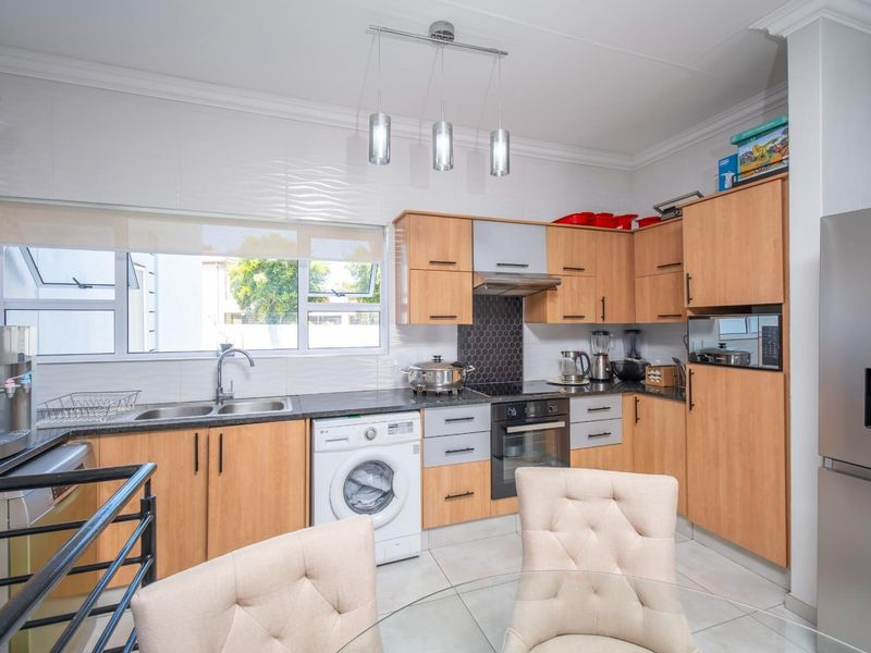 A functional kitchen featuring light wood cabinetry, dark countertops, a tiled backsplash, and integrated appliances including an oven, hob, and extractor fan.