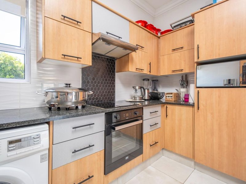 A functional kitchen featuring light wood cabinetry, granite countertops, a modern hexagonal tile backsplash, and integrated appliances including an oven and hob.