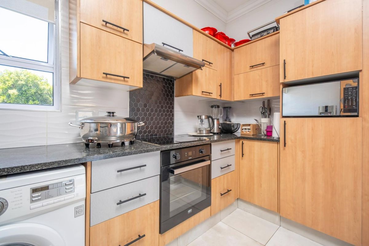 A functional kitchen featuring light wood cabinetry, granite countertops, a modern hexagonal tile backsplash, and integrated appliances including an oven and hob.