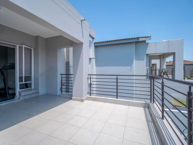 A spacious, modern covered balcony featuring neutral floor tiles and a secure metal balustrade, offering a clean and functional outdoor living space.
