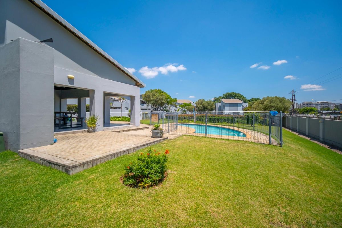 Rear exterior view featuring a covered patio, paved terrace, swimming pool with safety fencing, and a well-maintained lawn area.