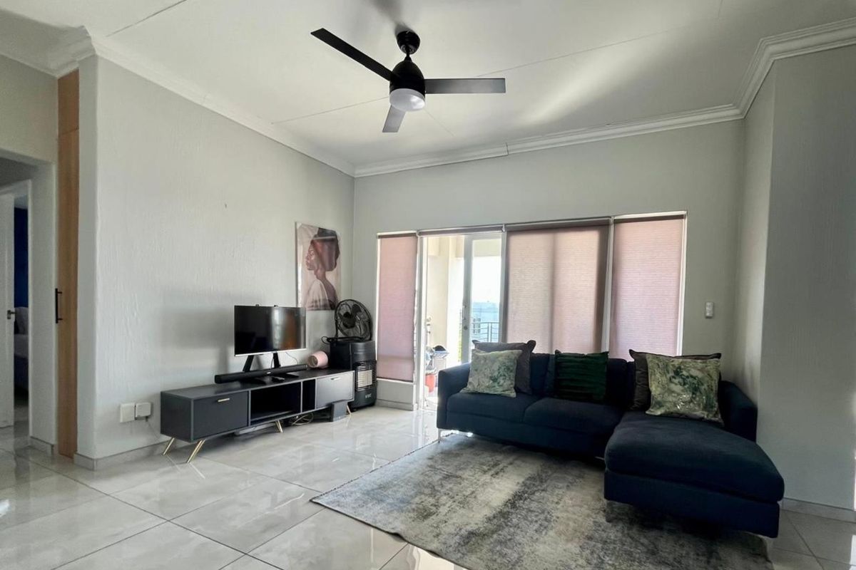 A bright living room featuring large format floor tiles, a modern ceiling fan, and sliding glass doors leading to an outdoor balcony area.