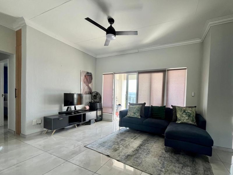 A bright living room featuring large format floor tiles, a modern ceiling fan, and sliding glass doors leading to an outdoor balcony area.