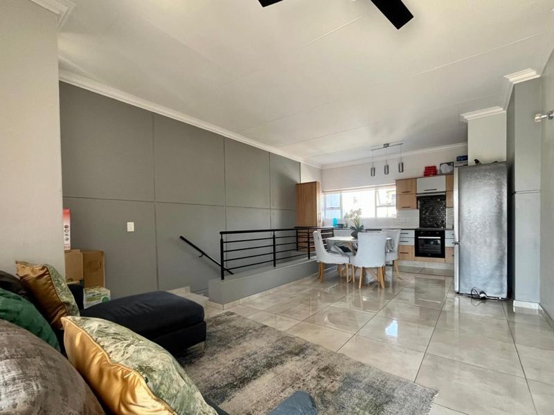 Open-plan living and kitchen area featuring tiled flooring, modern cabinetry, built-in oven, and a staircase with a metal railing.
