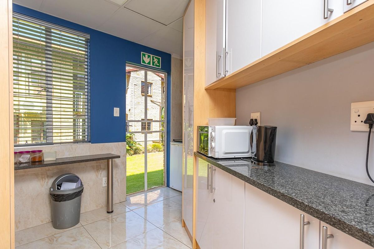 A functional office kitchenette featuring granite countertops, built-in cabinetry, tiled flooring, and direct access to an outdoor area.