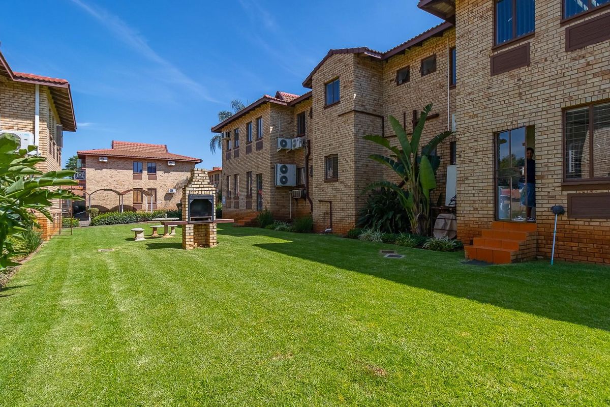 A well-maintained communal garden area featuring a brick-built braai facility, surrounded by face-brick office building facades with integrated air conditioning units.
