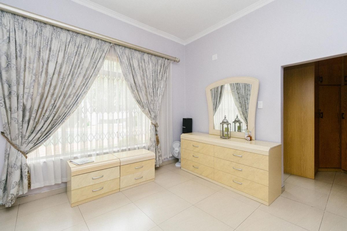 A well-maintained bedroom featuring neutral tiled flooring, coving, and a large window fitted with a security gate.