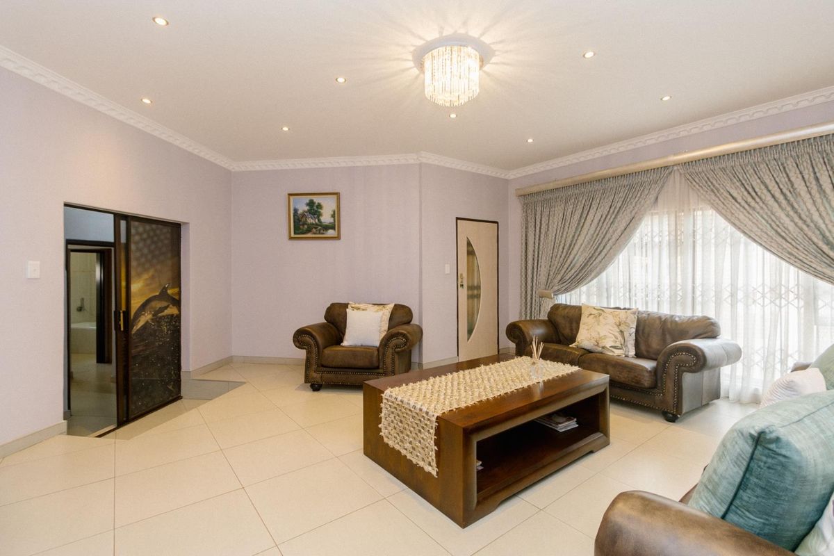 A well-maintained living room featuring tiled flooring, crown molding, recessed downlights, and a decorative crystal chandelier.