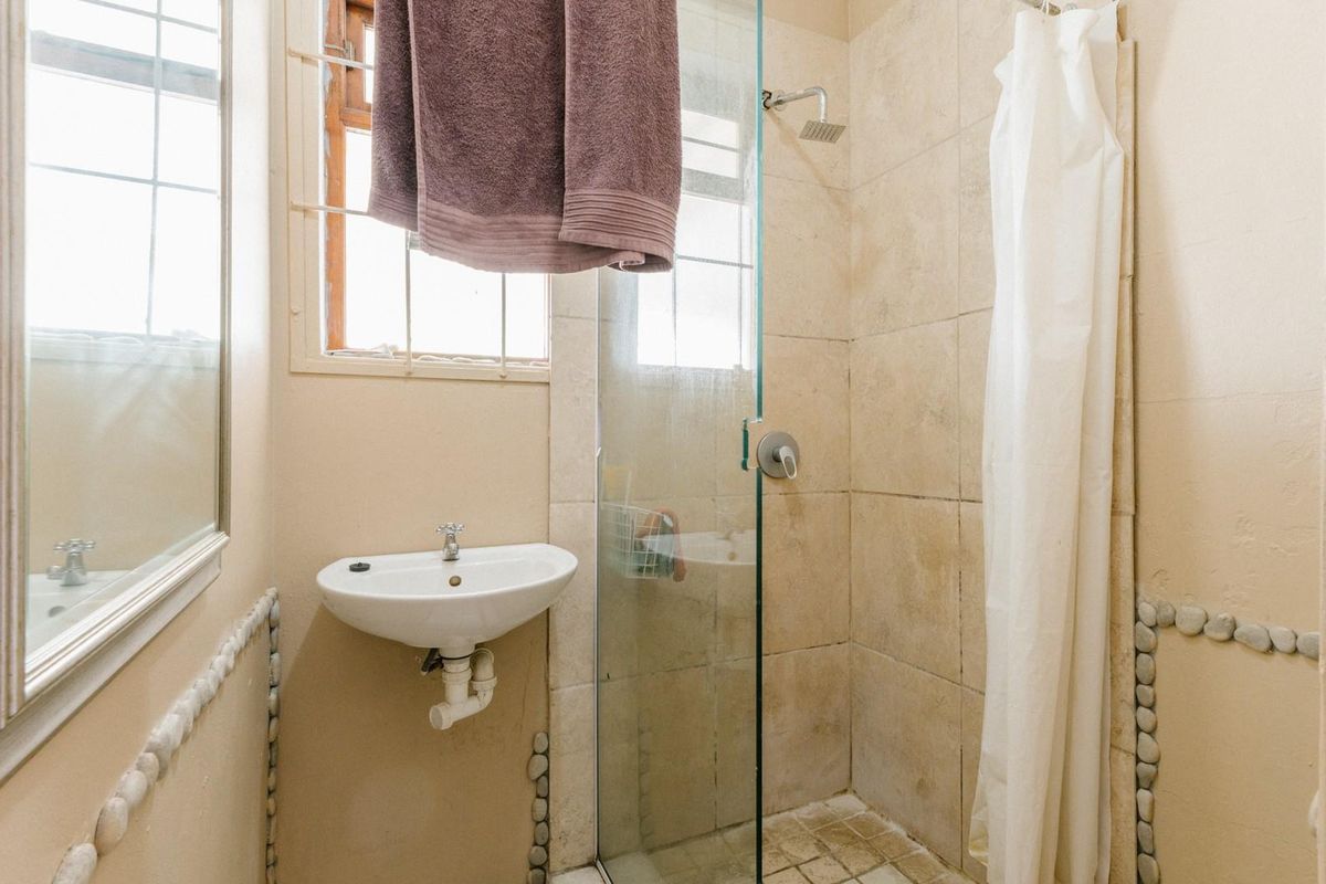 A compact bathroom featuring a wall-mounted basin, a tiled shower enclosure with a glass door, and decorative pebble-style wall accents.