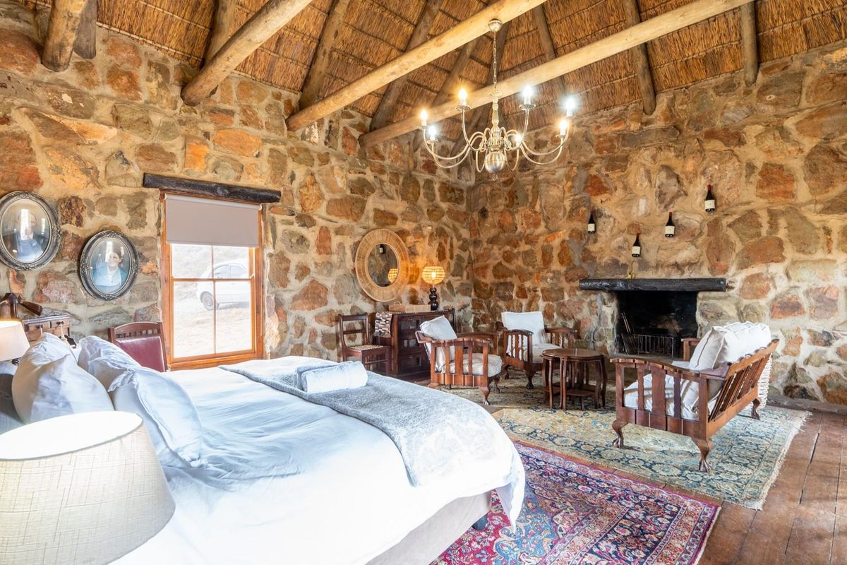 Rustic bedroom featuring exposed stone walls, a high thatched roof with timber beams, and a traditional open fireplace.