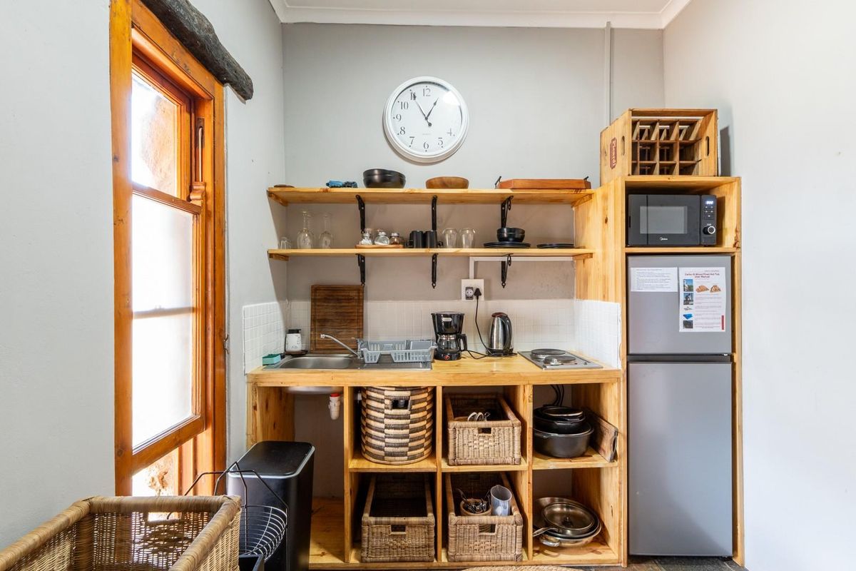 A compact kitchenette featuring open timber shelving, a built-in sink, a small electric cooktop, and integrated storage space.