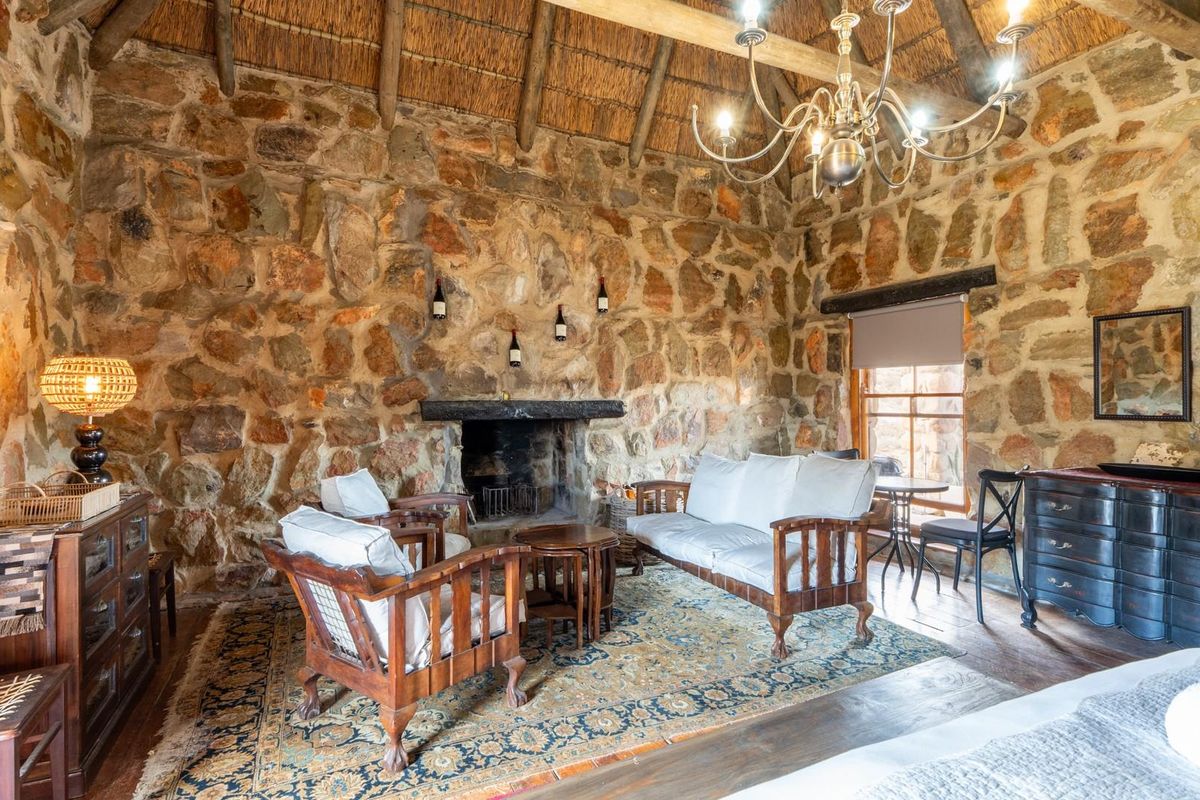 Rustic living area featuring exposed natural stone walls, a traditional stone fireplace, and a high-pitched thatched roof with exposed timber beams.