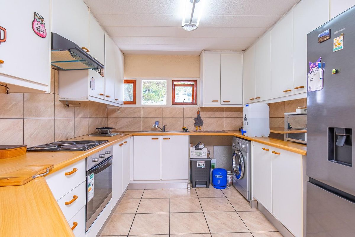 Functional kitchen featuring built-in cabinetry, integrated oven and hob, extractor fan, tiled backsplash, and dedicated space for laundry appliances.